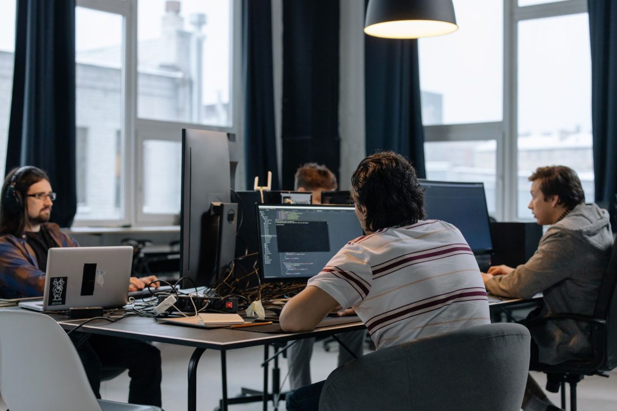 Software developers working at desks with laptops and monitors showing code in an office
